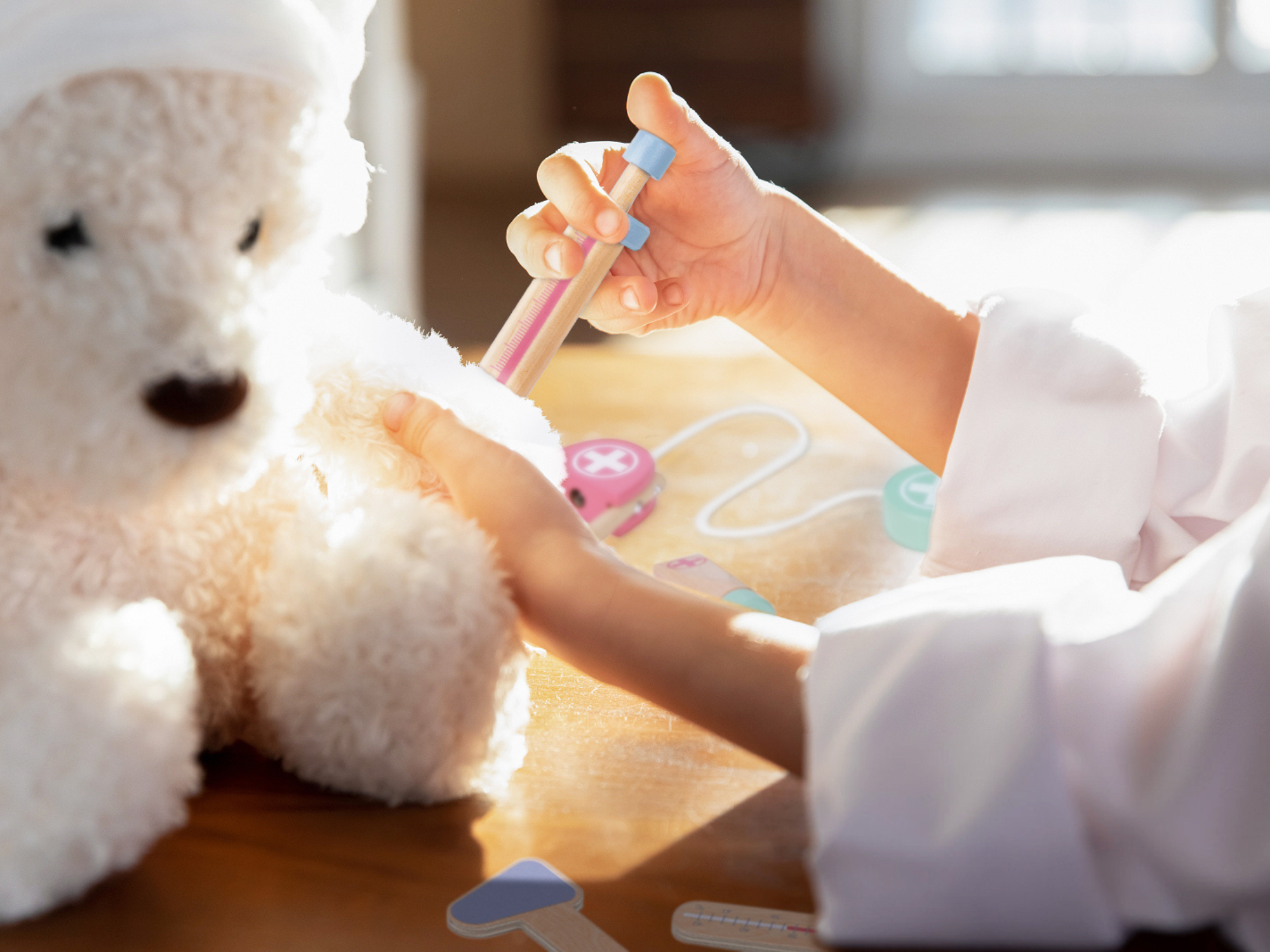 Djevojčica koja se igra sa setom za doktore i koristi dječju drvenu špricu na svom plišanom medi, fokusirana na zadatak
